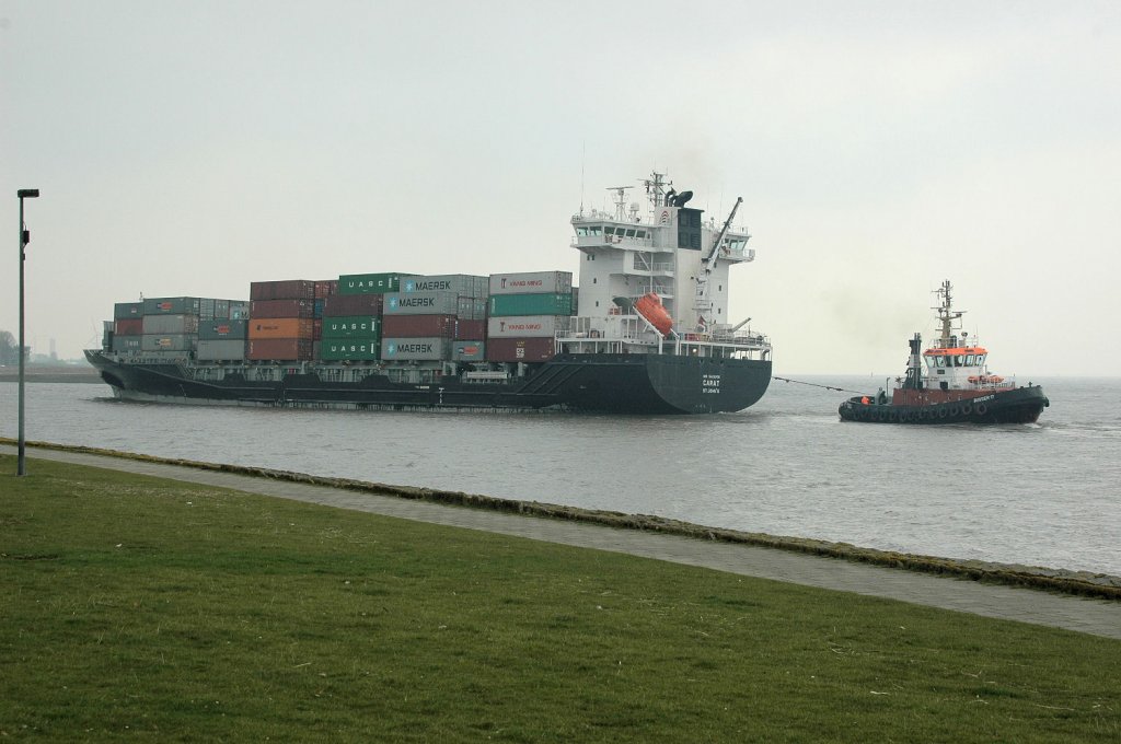Das in China 2009 gebaute Containerschiff Carat  (IMO: 9429209) mit einer Lnge von 141m, einer Breite von 23m und einem Tiefgang von7,90m aus Hamburg kommend, hier zur Einfahrt in die NOK-Schleuse Brunsbttel. Der Schlepper Bugsier 17 hinten dran, um die Richtung zu halten. Gesehen am 4.4.2011.