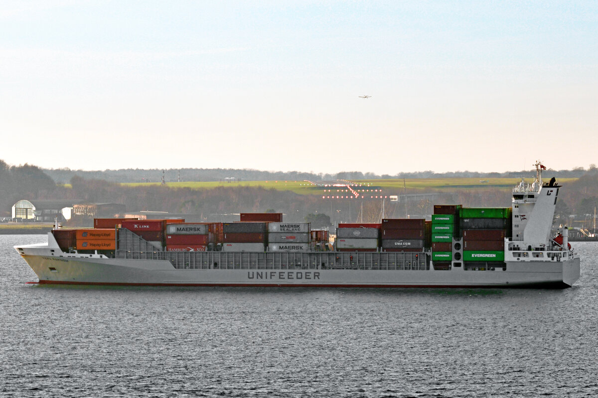 VERA RAMBOW (IMO 9432220) am 08.02.2023 in der Kieler Förde. Das Containerschiff befindet sich in Höhe des Flughafens Kiel, über dem ein Sportflugzeug zu sehen ist
