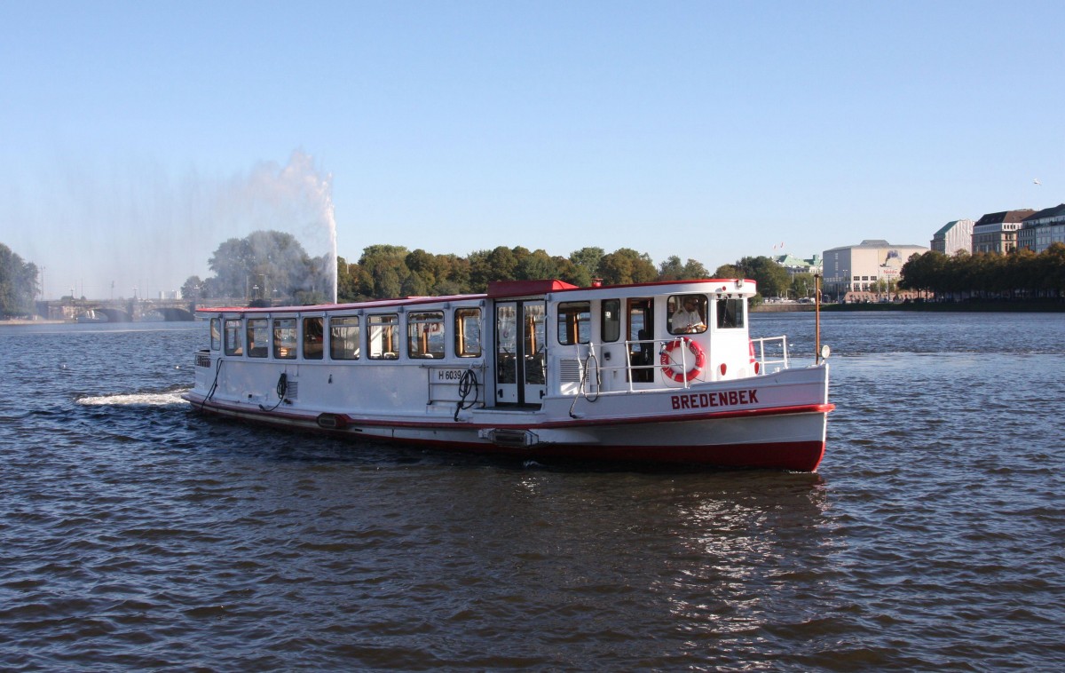 Am 11.10.2015 erreicht hier gerade das Rundfahrtschiff  Bredenbeck  den Anlieger Jungfernstieg an der Binnenalster in Hamburg. - Im Hintergrund steigt die Wasserfontäne empor und täuscht so einen mächtigen Auspuffstrahl vor. 