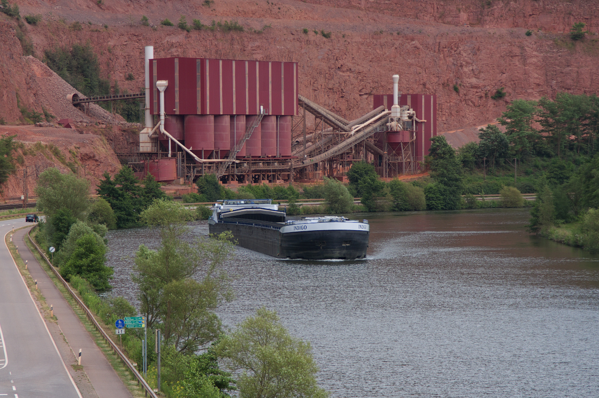 Am 15.06.2014 waren wir mal wieder im unteren Saartal unterwegs. Die DÜRO Hartsteinwerke bei Taben bieten immer eine tolle Kulisse. Das Frachtschiff MS INDIGO ist Saar abwärts unterwegs. In wenigen Kilometern wird das Schiff die Schleuse in Serrig erreichen, dort geht es tief bergab!!! Die Staustufe Serrig ist Deutschlands größte Flussstaustufe an einem natürlichen Flusslauf. Die Staustufe Serrig wurde in den Jahren 1981 bis 1986 erbaut und erreicht eine Hubhöhe von 14,5 m. Die Indigo wurde 2005 gebaut, ist 110 Meter lang und 11,45 Meter breit. Als Antrieb dient ein Caterpillar 1699 pk