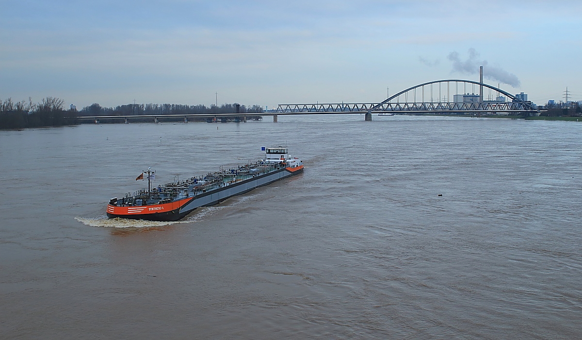 Am Mittag des 08.01.2018 hatte das Rheinhochwasser bei Düsseldorf einen Stand von etwa 830 cm erreicht. Ab Köln war die Schifffahrt bereits eingestellt, dies ist in Düsseldorf jedoch erst ab einem Pegelstand von 880 cm der Fall und so kämpfte sich TMS Synthese-4 (Druthen/NL, Länge: 97,70 m, Breite: 9,50 m, 1.707 t, 1.017 PS) langsam Richtung Süden. Im Hintergrund ist die Eisenbahnbrücke Neuss-Düsseldorf zu erkennen.