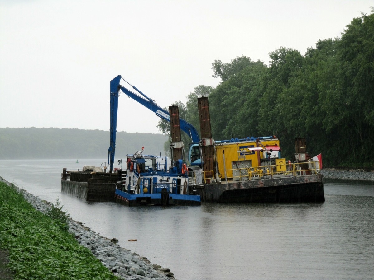 Bei strömendem Regen nimmt der Bagger auf der Arbeitsplattform Alpine 20 (04808250) seine Arbeit auf und nimmt das Material aus dem Leichter und verbringt dies auf den Grund des Sacrow-Paretzer-Kanal's. Potsdam/Nedlitz am 24.06.2014