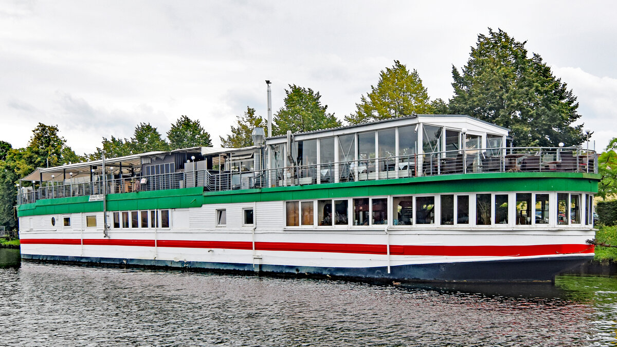 Das Betonschiff RIVERBOAT am 14.08.2021 in Lübeck. Es befindet sich seit den 1950er-Jahren in der Hansestadt und ist 55 Meter lang und 7,5 Meter breit. Es wurde 1942 von DYWIDAG (Dyckerhoff & Widmann) in Holland gebaut. Dieses Schiff bzw. dieser  Schwimmkörper , wie es korrekt heißen muss, denn es verfügte nie über einen eigenen Antrieb, wurde ausschließlich geschleppt und sollte schweres Kriegsgerät über den Kanal bringen. Nach Ende des Zweiten Weltkriegs diente es als Auffangstation für Flüchtlinge. 1956 wurde es unter der Lübecker Puppenbrücke vertäut und als Musikschiff (vor allem Jazz) eröffnet. 1978 wurde das Schiff auf die andere Seite des Holstentores, in den Holstenhafen, verbracht und als Diskothek wiedereröffnet. Als nach mehreren Anläufen auch hier der Erfolg langsam ausblieb, wurde das RIVERBOAT ein weiteres Mal verlegt;in den Klughafen (1994). Nach großen Umbau- und Sanierungsmaßnahmen öffnete im April 2007 das  neue  RIVERBOAT, jedoch nicht mehr als Diskothek, sondern als Veranstaltungszentrum. Das Restaurant  Seaside  bietet hier nunmehr  italienische Küche 