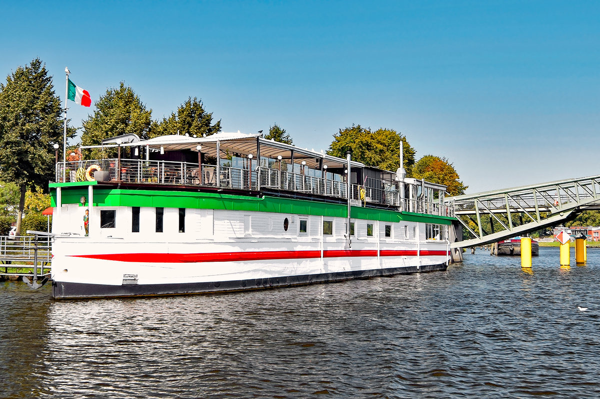 Das Betonschiff RIVERBOAT befindet sich seit den 1950er-Jahren in der Hansestadt Lübeck.Es ist 55 Meter lang und 7,5 Meter breit. 1942 von DYWIDAG (Dyckerhoff & Widmann) in Holland gebaut, diente es nach dem Krieg als Auffangstation für Flüchtlinge. 1956 wurde es unter der Lübecker Puppenbrücke vertäut und als Musikschiff (vor allem Jazz)eröffnet. 1978 wurde das Schiff auf die andere Seite des Holstentores, in den Holstenhafen, verbracht und als Diskothek wiedereröffnet. Als nach mehreren Anläufen auch hier der Erfolg langsam ausblieb, wurde das RIVERBOAT ein weiteres Mal verlegt;in den Klughafen (1994). Nach großen Umbau- und Sanierungsmaßnahmen öffnete im April 2007 das  neue  RIVERBOAT, jedoch nicht mehr als Diskothek, sondern als Veranstaltungszentrum. Das Restaurant  Seaside  bietet hier nunmehr  italienische Küche .

Aufnahme vom 26.08.2016
