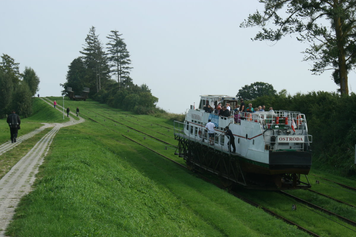 Die Gesellschaft Żegluga Ostródzko-Elbląska führt den touristischen Betrieb auf dem Oberländischen Kanal durch. Sie wirbt mit dem Slogan,  Mit dem Schiff über die Wiese.  Dabei kann man die Strecke von Elblag nach Buczyniec fahren oder nur eine Kurztrip von Buczyniec nach Olesnica über drei Rollberge machen. Mit der Fahrt von Elblag nach Buczyniec erfüllte ich mir am 09.09.2017 einen langen Kindheitstraum.
Auf dem Foto wird die M/S  Ostroda  über den Rollberg Jelenie transportiert. Das Schiff überwindet auf 433 m Länge einen Höhenunterschied von 22 m. Jelenie, 09.09.2017