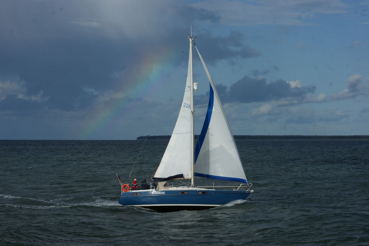 Ein kleines Segelboot zeigt sich am 10.08.2016 in der Warnowmündung in Warnemünde vor einem schönen Regenbogen.