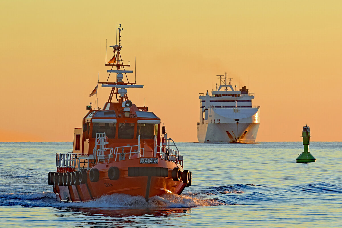 Lotsenversetzboot BÜLK im Licht der aufgehenden Sonne in der Ostsee vor Lübeck-Travemünde. Im Hintergrund ist das Frachtschiff CADENA 3 zu sehen.August 2022