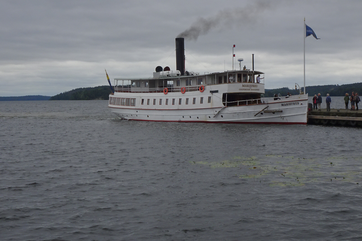 Nach dreieinhalb-stündiger Fahrt von Stockholm über den Mälaren hat der Dampfer Mariefred (Reederei Stromma)seine namensgebende Stadt erreicht, die Passagiere gehen von Bord. Der Kapitän beobachtet das von der Brücke aus, der Heizer hat noch einmal tüchtig Kohle aufgelegt. 
Das Dampfschiff bewegt sich lautlos über den See, nur das Rauschen des Wassers ist zu hören. Steht man vor dem Maschinenraum, so ist die Dampfmaschine nicht lauter als eine Nähmaschine.
Welch wohltuende Ruhe in dieser lauten Zeit!
Mariefred, Schweden, Samstag, 26. August 2023