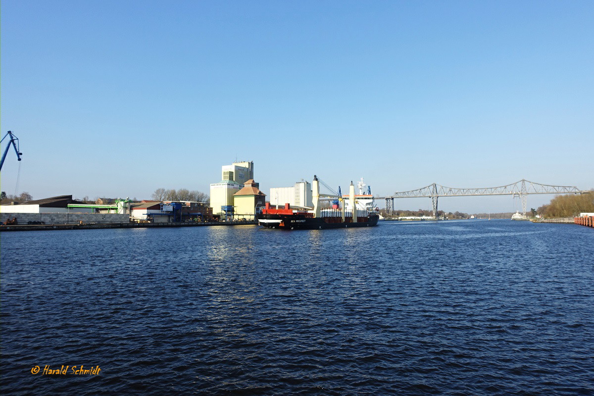 Nord Ostsee Kanal am 10.4.2023 Höhe Hafen Rendsburg mit einem Teil der Eisenbahnhochbrücke und dem aufkommenden, tief abgeladenem Mehrzweckfrachter SEA PROSPECT von Kiel/Ostsee kommend  /