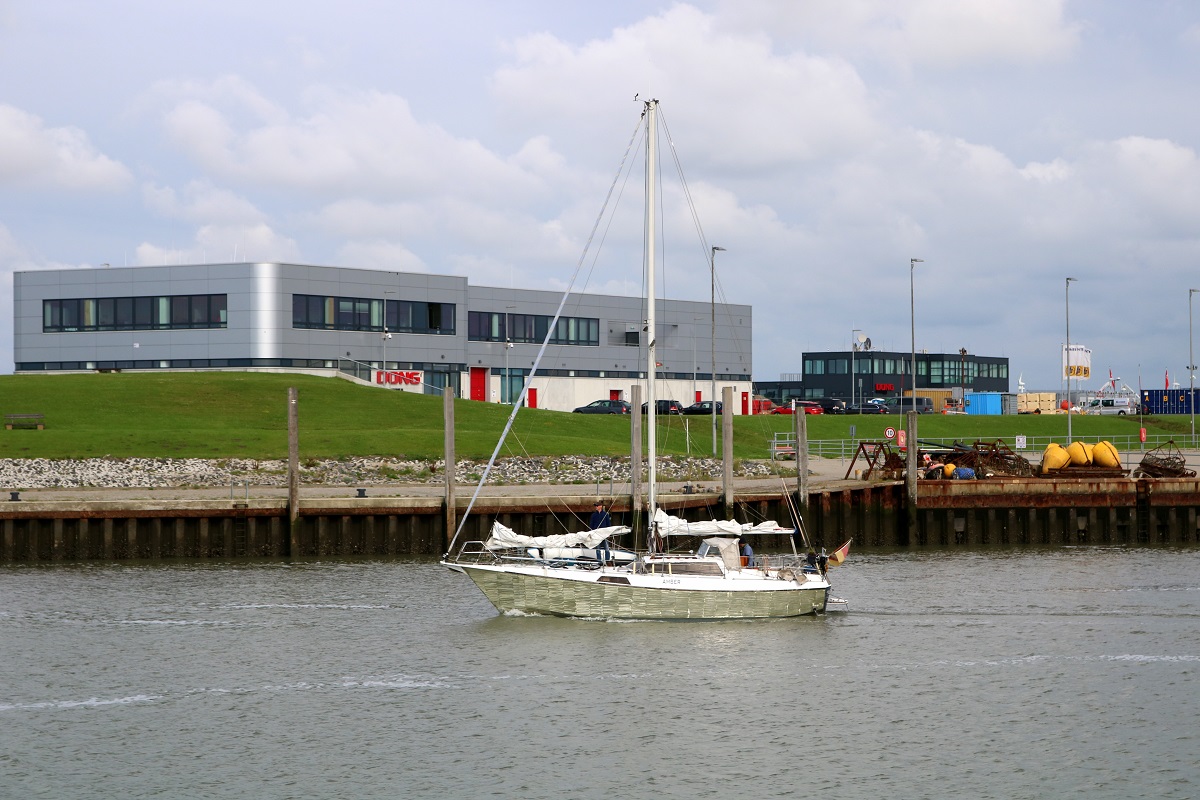 Segelboot  AMBER  läuft aus dem Norddeicher Hafen aus. Im Hintergrund ist das Gebäude von DONG Energy zu sehen. [24.7.2017 - 17:11 Uhr]