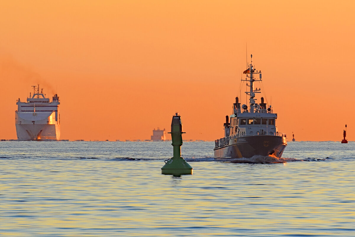 Zollboot PRIWALL und das Frachtschiff CADENA 3 im Licht der aufgehenden Sonne in der Ostsee vor Travemünde. August 2022