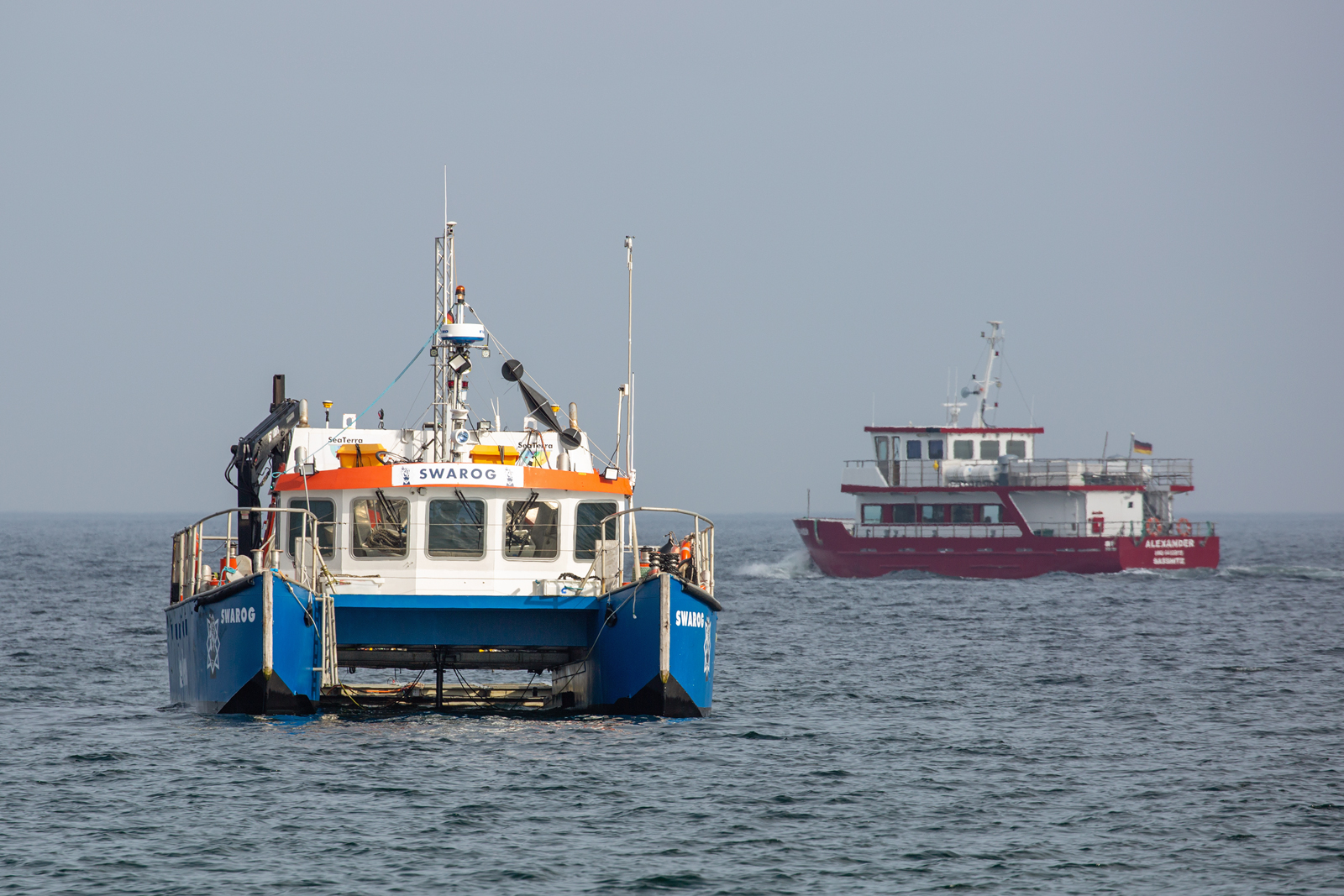 Die SWAROG der Sea Terra scheinbar bei Unterwasserarbeiten vor der Sassnitzer Ostmole. Im Hintergrund fährt das Fahrgast Schiff ALEXANDER zu einem Bestimmten Punkt auf der Ostsee. - 31.03.2023 
