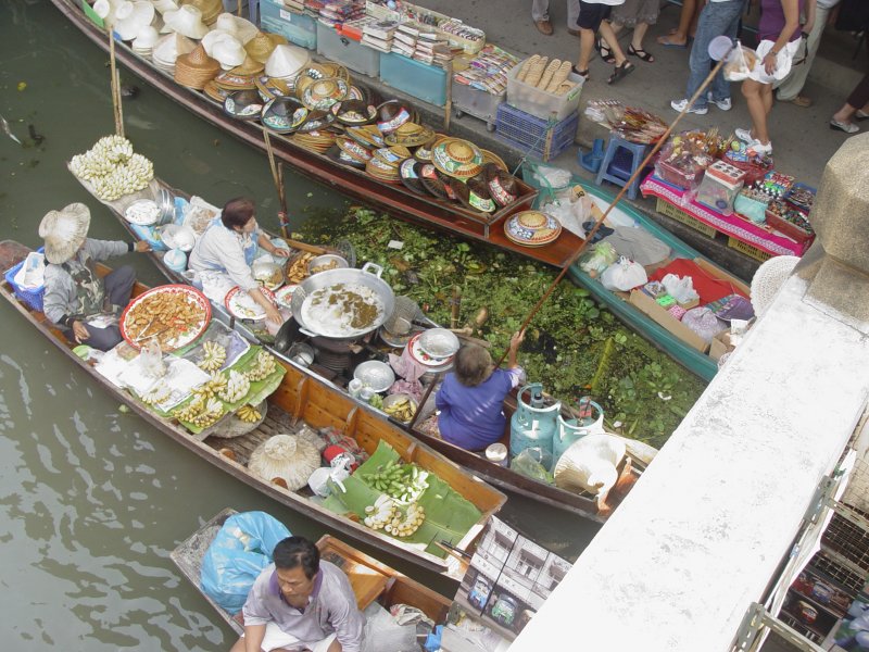 Auf dem Floating Market von Damnoen Saduak hat der Besucher von einer Halbbrcke ber einen der Kanle aus eine Blick von oben auf die unter ihm dahin gleitenden bzw. liegenden Ruderboote, von denen aus, wie hier zu sehen, Obst und Sonnenschutzhte verkauft werden, aber auch eine Garkche ist hier zu sehen. (27.01.2009)