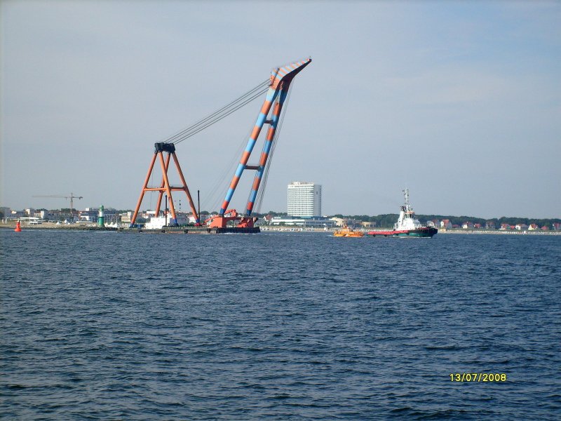 Schlepper  Asterix , HH Aarhus, OXLL2, IMO 9280433, im Anhang mit Schwimmkran  Samson  bei der Ausfahrt aus dem Hafen Rostock, im Hintergrund die Silhouette von Warnemnde mit dem Hotel Neptun (Bildmitte) 