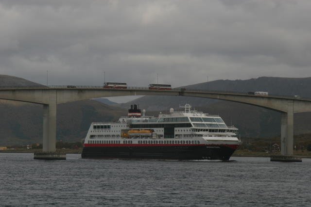 Tglich das selbe Bild vom perfekten Timing. Whrend die sdgehende M/S  Trollfjord  unter der Sortlanbru hindurchfhrt, fahren die Ausflugsbusse mit interessierten Hurtigrutenpassagieren ber ihr Schiff hinweg. Die Busse befinden sich auf dem Versterlen-Landausflug von Harstad nach Sortland. Natrlich wird sich bei dieser Begegnung mit  dreimal lang  gegrt. Das Schiff mit dem Typhon, die Busse antworten mit ihrer Hupe.; 08.09.2006, sdgehend
