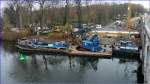 Arbeitsschute (ENI-Nr.05601930) der Fa.Mette, Wasserbau, als Arbeitsplattform fr einen Raupen-Drehkran. Am Arbeitsgeschirr hngt ein Vibrationsgert zum Einrtteln von Spundbohlen. Angedockt hat das Schubboot (ENI-Nr.05601750)  TRAVE . Es finden Vorarbeiten fr den Bau einer Behelfsbrcke (temporrer Ersatzbau fr die Freybrcke) ber die Untere Havel-Wasserstrae statt. Im Bildhintergrund erkennt man (der helle horizontale Riegel) den Baubeginn fr ein Behelfs-Brckenlager. Foto:18.11.2013  