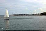 Blick während einer Hafenrundfahrt auf den Yacht- und Gewerbehafen des Ostseebads Laboe mit Segelboot im Vorder- und Marine-Ehrenmal im Hintergrund.