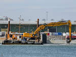 Der Bagger auf dem Ponton MP 36 bei der Arbeit, so gesehen Anfang Mai 2023 in Travemünde.