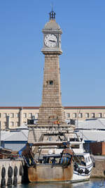Im Bild ein Fischereischiff vor dem 1772 ursprünglich als Leuchtturm gebauten Uhrenturm Torre del Rellotge in Barcelona. (November 2022)