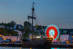 Pommernkogge UCRA der Stadt Torgelow liegend im Sassnitzer Hafen mit beleuchtetem Riesenrad im Hintergrund. - 09.07.2023





