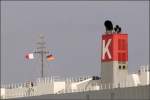 Die wei-rote Flagge neben der Deutschlandflagge bedeutet: Lotse an Bord. Sie steht auch fr den Buchstaben H (Hotel). Die Schornsteinmarke mit dem weien K auf rotem Grund kennzeichnet die Reederei K-Line. Gesehen am 30.03.2010 auf der SOUTHERN HIGHWAY in Bremerhaven.
