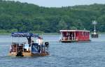 Begegnung auf der Unterhavel. Das Floß im Vordergrund wird von einem Bootsverleih aus Berlin-Spandau verchartert. Es verfügt über einen 9,9PS  Mercury Motor. Entgegen kommt ein Hausboot der Fa.BunBo (Bungalow Boot). Daten zum schwimmende Ferienhaus: L=11,6m; Breite=4,65m;Tiefgang=0,65m. Antrieb wahlweise mit 15 oder 20PS; Vmarsch.7-9km/h. Wohnbereich, Badezimmer, WC, Küche, 2 Schlafzimmer. Foto:25.06.2015 