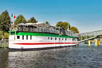 Das Betonschiff RIVERBOAT befindet sich seit den 1950er-Jahren in der Hansestadt Lübeck.Es ist 55 Meter lang und 7,5 Meter breit. 1942 von DYWIDAG (Dyckerhoff & Widmann) in Holland gebaut, diente es nach dem Krieg als Auffangstation für Flüchtlinge. 1956 wurde es unter der Lübecker Puppenbrücke vertäut und als Musikschiff (vor allem Jazz)eröffnet. 1978 wurde das Schiff auf die andere Seite des Holstentores, in den Holstenhafen, verbracht und als Diskothek wiedereröffnet. Als nach mehreren Anläufen auch hier der Erfolg langsam ausblieb, wurde das RIVERBOAT ein weiteres Mal verlegt;in den Klughafen (1994). Nach großen Umbau- und Sanierungsmaßnahmen öffnete im April 2007 das  neue  RIVERBOAT, jedoch nicht mehr als Diskothek, sondern als Veranstaltungszentrum. Das Restaurant  Seaside  bietet hier nunmehr  italienische Küche .

Aufnahme vom 26.08.2016
