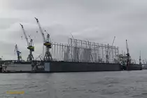 Blohm + Voss Dock 10 am 28.1.2021 mit dem im Bau befindlichen Gerüst für die Überdeckung des Docks, es entsteht für 13 Mio. Euro eines der größten schwimmenden Schiffbauhallen Europas,  3 Fassadenseiten werden mit Blechplatten verkleidet, die zur Wasserseite zeigende Seite wird mit einer millimeterdünnen dauerhaften Folie bespannt, sodaß ein riesiges „Schaufenster“ entsteht  durch das man den Arbeitern beim Arbeiten zusehen kann /

Schwimmdock / L 287,5 m, B 44,2 m, Tg 10,21 m / für Schiffe bis 130.000 dwt / Hebekapazität: 50.000 t / Kräne: 2 x 35 t, 2 x 15 t /
