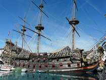 In Genua liegt der Nachbau einer Galeone mit Namen  Neptuno , so steht es zumindest auf der Schiffsglocke. In anderen Quellen wird das Schiff auch  Les Neptunes  genannt.
Leider habe ich es auch mit Weitwinkel nicht ganz auf das Foto bekommen.
Dieses Schiff war neben Walter Matthau die Hauptdarstellerin im Film  Piraten  von Roman Polanski.
Es wurde Anfang der 80iger Jahre erbaut. Zuerst ein st�hlerner Rohbau in Malta, welcher sp�ter in Tunesien ausgebaut wurde und dabei vollst�ndig mit Iroko-Holz verkleidet diesen doch recht echt wirkenden Nachbau ergab. Zwei Jahre lang fanden 2000 Bootsbauer und Tischer hiermit ihre Besch�ftigung, im Umfeld arbeiteten zeitweise sogar bis zu 10 000 Tunesier. Am Ende hatte dieser Nachbau 8,2 Millionen Dollar (damals fast 16 Millionen Deutsche Mark) gekostet. Auf Grund dieser Bausumme und weil das Schiff ja so wichtig f�r das Film-Projekt war, wollte man es nat�rlich auch versichern. Nach langen Verhandlungen erkl�rte sich Lloyd´s in London bereit, das Schiff f�r 30 Millionen Dollar zu versichern. Seitdem gibt es bei Lloyds auch wieder eine Akte �ber eine Galeone. Nach Ende der Dreharbeiten wollte Roman Polanski das Schiff behalten. Die Unterhaltskosten wurden aber so hoch, dass er es am Ende verschenken musste, weil kein K�ufer zu finden war. Das Schiff befand sich ohnehin in Cannes, anl�sslich der Filmfestspiele und so nahm die Stadt Cannes dieses Geschenk dankend an und machte daraus ein Museumsschiff. Anfangs besuchten Tausende Woche f�r Woche das Schiff. Scheinbar lie�en die Besucherzahlen aber sp�ter stark nach und das Schiff gelangte nach Genua, wo es immer noch als Museum dient. 
Nun noch einige Technische Daten: L�nge �ber alles 62 Meter, Breite 16,4 Meter, 4500 Quadratmeter Segelfl�che, 1500 Tonnen Gewicht und urspr�nglich mit zwei Maschinen von je 400 PS ausgestattet. Damit erreichte es eine Geschwindigkeit von f�nf Knoten, nicht besonders schnell aber ausreichend f�r die Dreharbeiten.